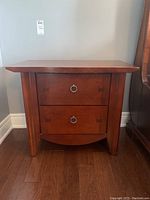 Front view of one wooden side table showing two drawers with metal ring pull handles and bow-tie inlay accents.