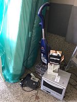 Overall view of Bissell steam cleaner standing upright next to Panasonic toaster oven, Kwikset door lock box, and black phone on floor.