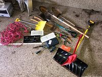 Full view of all tools including shovels, hand tools, and extension cord on garage floor
