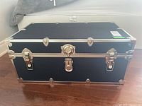 Front view of the black wood trunk showing its rectangular shape and metal hardware.