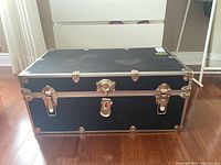 Photo of full black wood trunk with metal hardware placed on wood floor