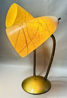 Front view showing yellowish fibreglass shades lit up with abstract brown lines, bronze base and flexible gooseneck arms.