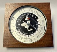 Front view of the Seiko quartz world time clock showing the wood frame, 24-hour dial with city names, red airplane second hand, and map design.