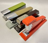 Four vintage metal staplers in a row showing colors and design