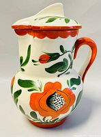 Front and side view showing the floral hand painted decoration, lid, and handle of the pitcher.