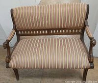 Front view of antique wooden bench with upholstered seat and backrest in striped fabric. Shows wear consistent with age.