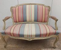 Front view of antique French loveseat showing carved wooden frame and striped upholstered seat and backrest.