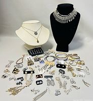 Wide view of entire jewelry lot including necklace displays, earrings on cards and loose, bangles, and bracelets arranged on table