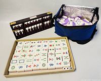 Photo showing complete mahjong tile set arranged neatly in a box with fabric storage bag of tiles and abacus behind it.