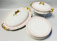 Six Limoges porcelain plates, two covered serving platters with lids showing gold and pink floral decoration.