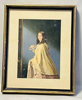 Framed Victorian print showing seated woman with yellow cloak and floral fan, with visible minor wear on frame edges