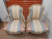 Front view of two antique wooden arm chairs with striped upholstery placed side by side