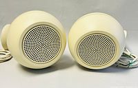 Front view of the two off-white vintage spherical speakers showing perforated metal grilles and attached power cords.
