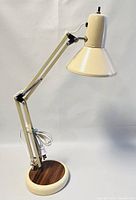 Full side view of the vintage adjustable desk lamp showing cream metal arms, lampshade, and wooden base with power cord coiled on base.