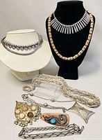 Full view of assorted metal necklaces and pendants arranged on display busts and flat surfaces showing variety of styles and materials.