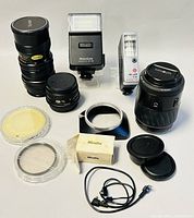Full view of vintage camera lenses, flashes, filters, and accessories arranged on a white background.