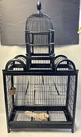 Front view of the full birdcage showing the top domed section and larger bottom section with metal bars and wooden frame, featuring a finial on top.