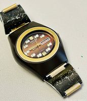 Front view of vintage Citizen wristwatch showing black case, gold-tone bezel, brown patina dial with day-date window and metal bracelet with scratches.