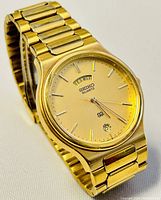 Front view of a vintage gold-tone Seiko Quartz men's wristwatch with visible day and date display, and gold dial and bracelet.