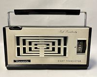 Front view of vintage NANAOLA transistor radio showing geometric speaker grill, tuning dial and carrying handle.