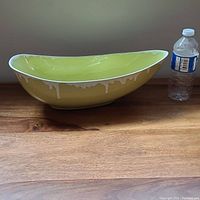 Side view of the elongated bowl on a wooden surface with a water bottle for scale