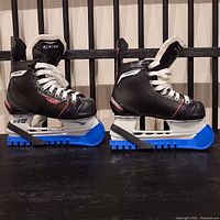 Pair of CCM kids ice skates size 13J with blue skate guards on black surface