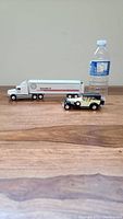 Schindler replica truck and antique-style toy car side by side with water bottle for size reference