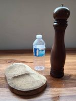 Olive wood tray and tall wood pepper mill next to water bottle for size reference.