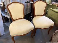 Two beige upholstered traditional accent chairs with wooden frames and curved legs. Chairs show general wear and tear.