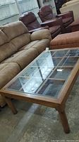 Full view of the coffee table showing the solid wood frame and clear glass top with surrounding furniture in the background.