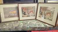 Three framed prints on table depicting deer themed Native and vintage art.