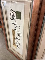 Two Ethan Allen framed prints leaning against a shelf, one glass intact and the other missing glass, showing abstract black floral shapes over geometric color blocks.