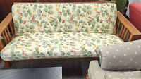 Full view of the wooden frame futon with floral patterned upholstered mattress and slipcover, showing the seat and backrest.