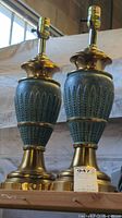 Full view of both vintage brass table lamps showing their painted slate blue bodies with wheat decoration and brass base and top, approximately 20 inches tall.