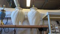 Pair of large white plaster table lamps with carved leaf-like design, no shades, on a wooden shelf under fluorescent lights.