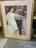 Photo of framed "Woman in White" print by Whistler showing woman in white dress holding a fan next to a mantel with vase and flowers.