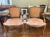 Pair of two matching wooden arm chairs with carved details and light brown upholstery, shown from front view.