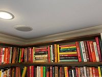 Bookshelves filled with hardcover fiction books by various authors including John Irving, James Patterson, Wilbur Smith. The books are arranged tightly on wooden shelves with visible color variation of book spines.