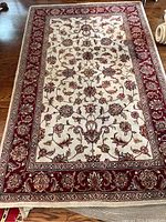 Full top view of rectangular floral area rug with cream center and burgundy border on wooden floor.