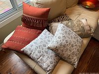 Photo showing all six cushions arranged on a beige couch near a window.