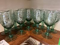 Set of 12 green stemmed glasses with textured pattern on bowl, arranged on wooden shelves.
