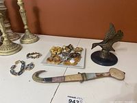 Several costume jewelry pieces grouped on a white plate, two pairs of clip-on earrings, and a decorative dagger and bronze bird paperweight on a white surface.