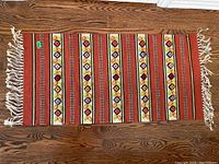 Full top-down view of rectangular kilim rug with warm red base and stripes with floral motifs, showing fringed ends.