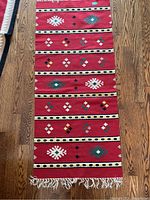Full view of a red kilim rug with multiple rows of geometric shapes and horizontal striped bands, showing the full length and tassels.
