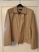Front view of beige leather jacket on hanger showing full length and collar.