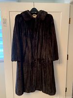 Front view of the fully closed dark brown mink fur coat hanging on a door, showing the entire length and collared neckline.