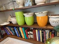 Shelf with various ceramic planters and decorative pots in green, orange, and white colors above a bookshelf.