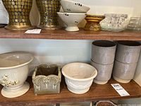 View of multiple ceramic planters arranged on shelves, showing variety of shapes, colors, and decorative styles.