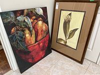 Two art pieces leaning against a wall: a colorful gallery stretched canvas painting of pears in a red bowl, and a framed botanical print titled 'Botanical II' by G. Ehret.