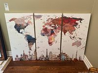 Full set of three canvas prints displayed leaning against a wall showing the entire world map and landmarks along bottom.